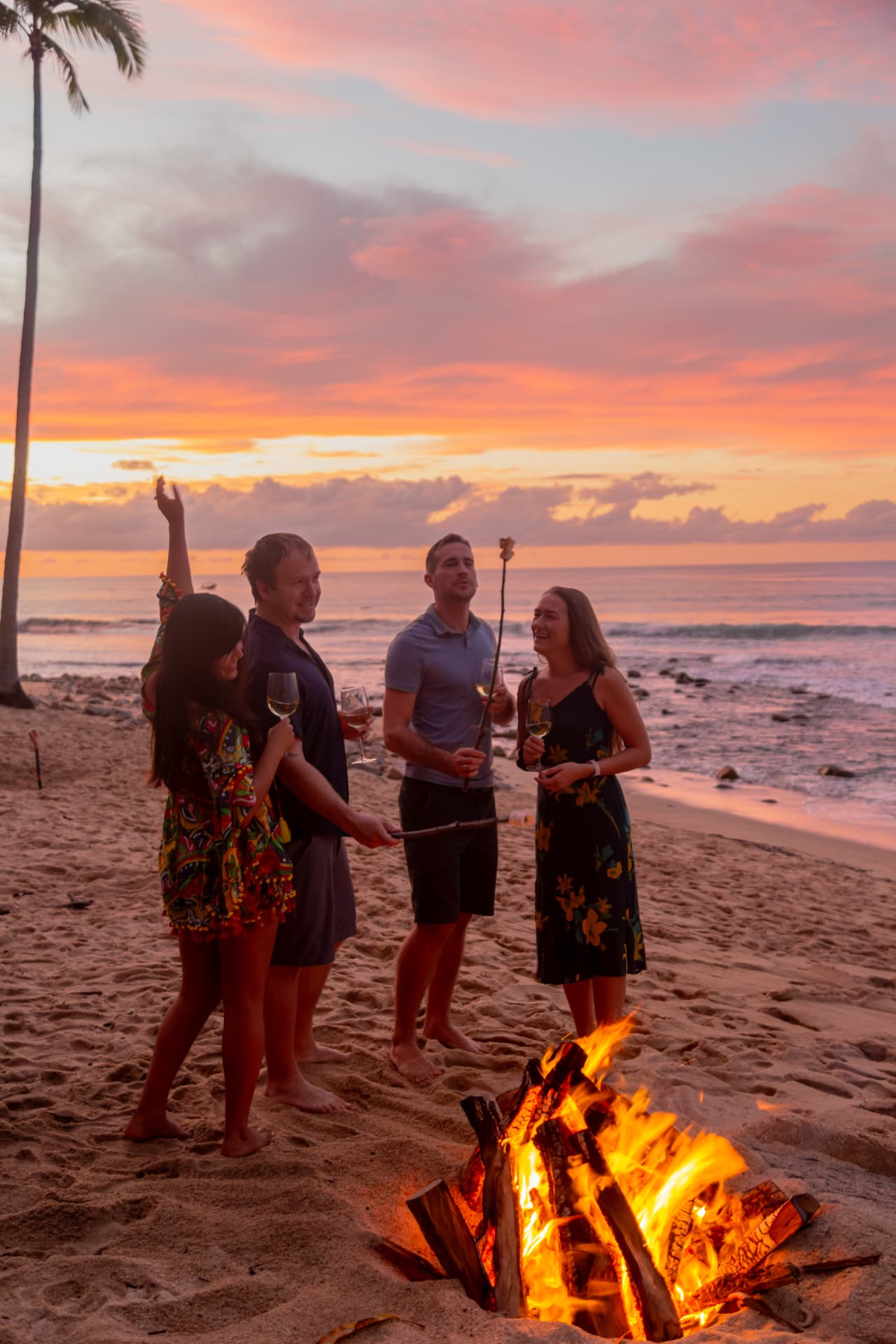 Group of friends around a bonfire on the beach at sunset