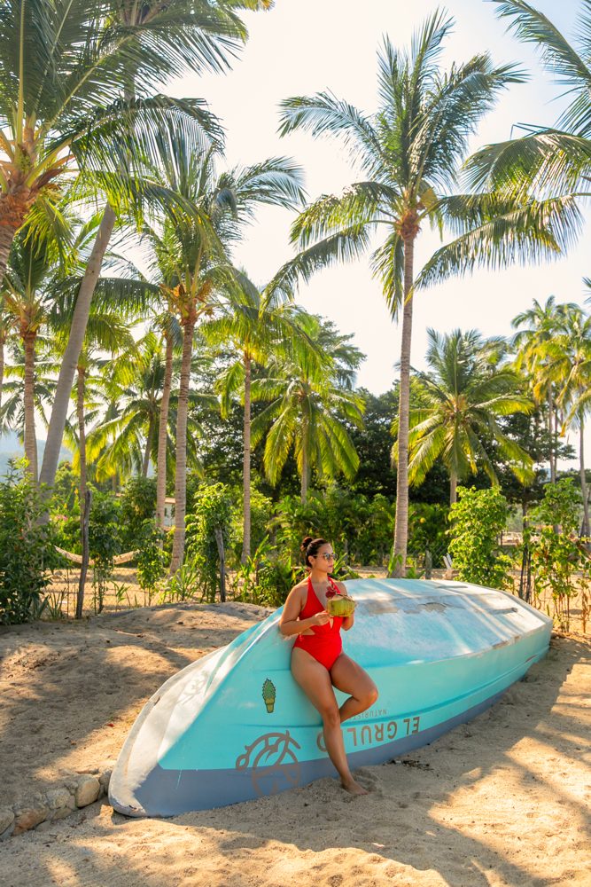 Solo traveler with a coconut beside a boat in Quimixto, Puerto Vallarta